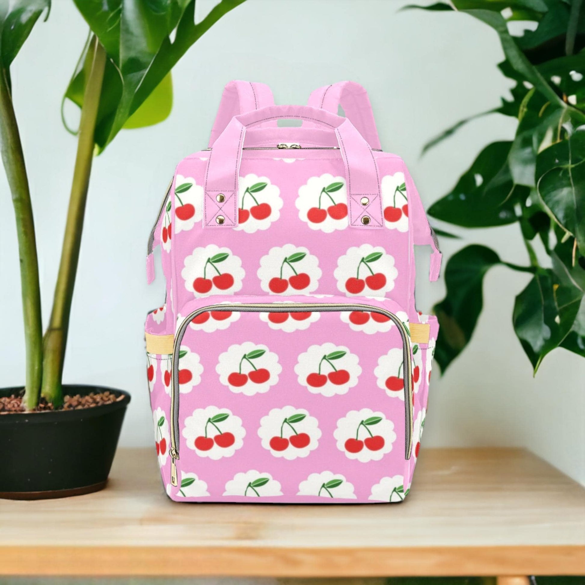 a pink backpack with cherries on it next to a potted plant