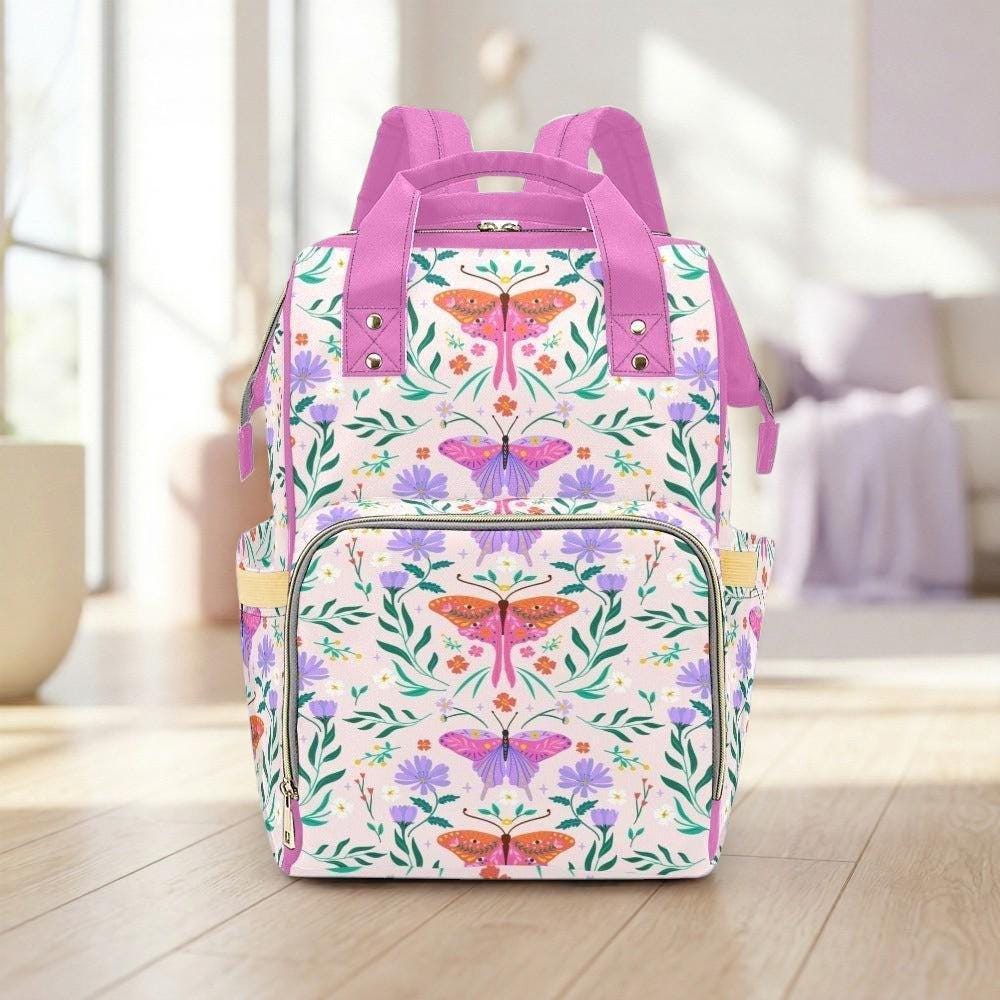 A colorful backpack with a floral pattern and butterflies printed on it, placed on a wooden floor in a room with a window.