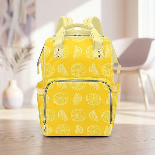 A yellow backpack with a pattern of lemon slices on it, placed on a wooden floor in a room with a white chair and a vase in the background.