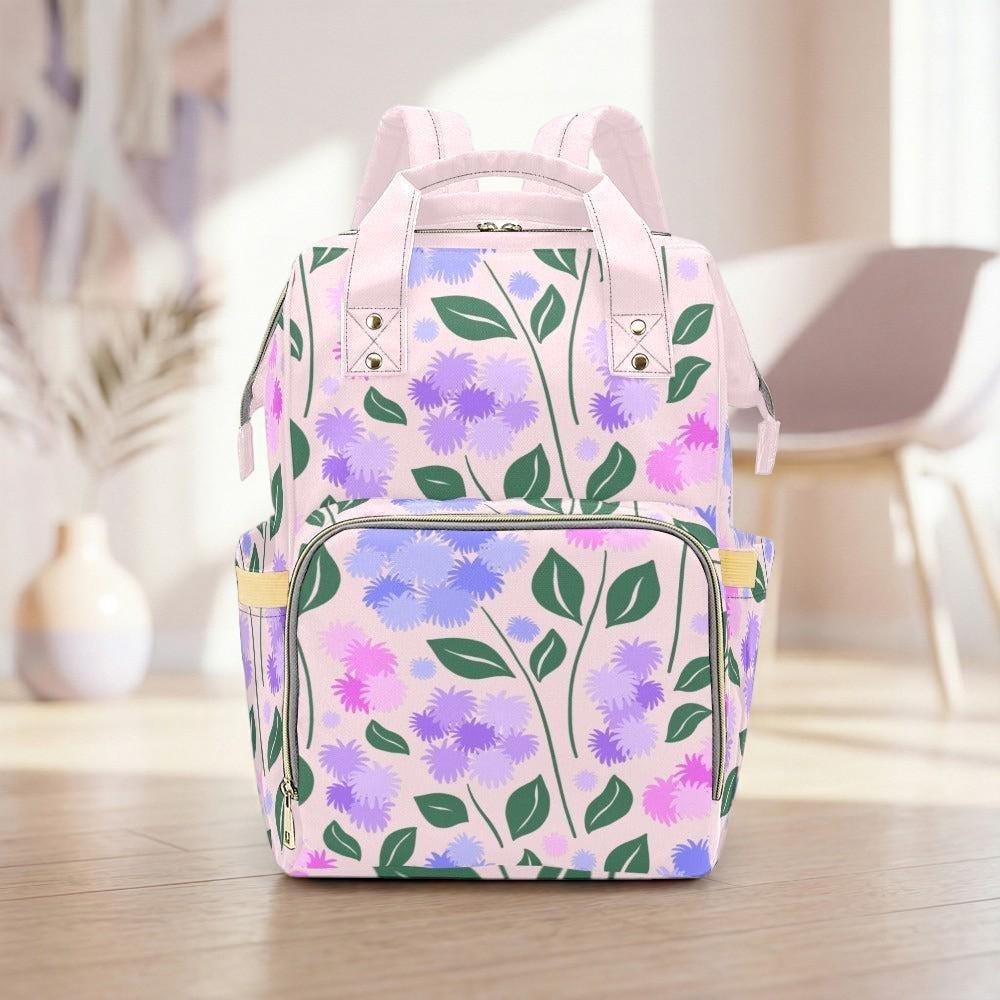 A pink and purple floral backpack with green leaves is displayed on a wooden floor in a room with a white chair and a vase in the background.