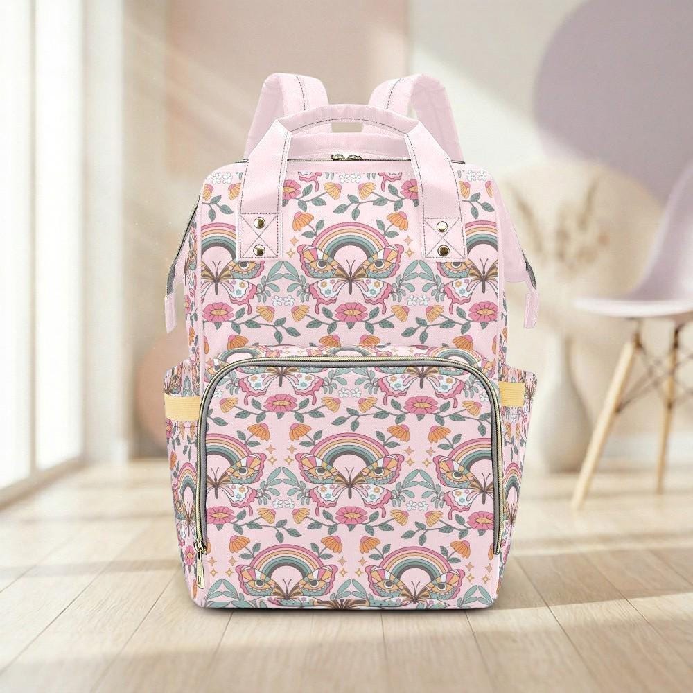 A pink and green floral backpack with a rainbow pattern is displayed on a wooden floor in a room with a chair and a window.