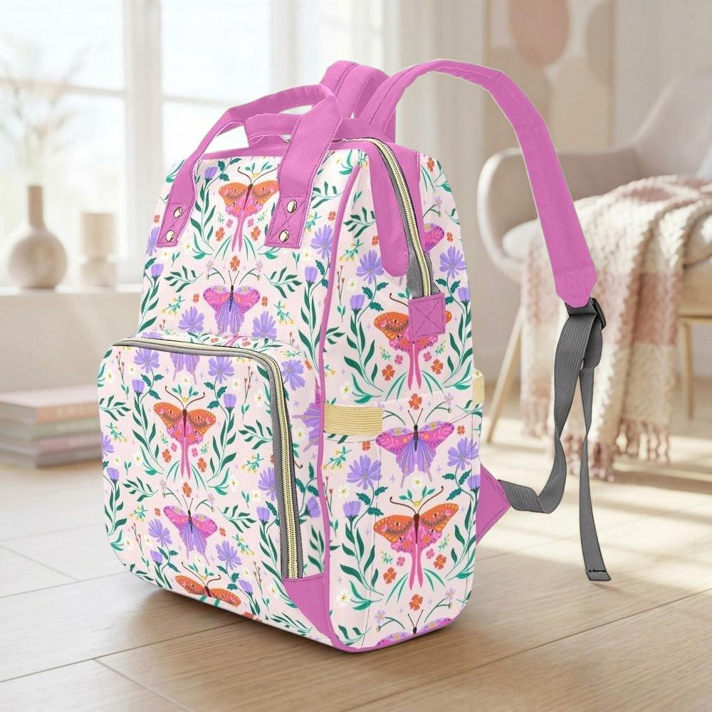 A colorful floral backpack with a pink strap is sitting on a wooden floor in a room with a window and a chair visible in the background.